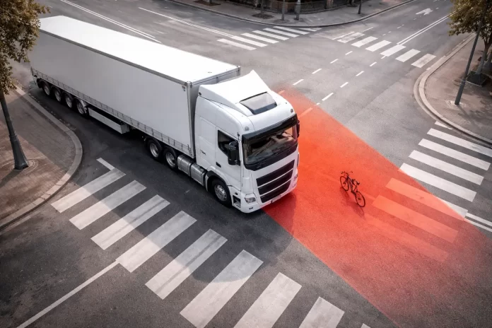 Vista dall'alto di un camion in svolta a destra con zona rossa che evidenzia l'angolo cieco dove si trova una bicicletta
