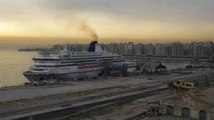 Nave ormeggiata in un porto italiano con pennacchio di fumo dalla ciminiera; sullo sfondo edifici residenziali affacciati sulla banchina.