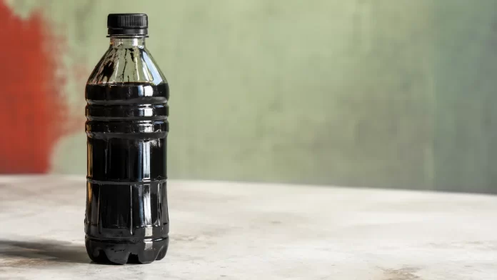 Bottiglia di plastica trasparente riempita di petrolio greggio nero, immagine simbolica del legame strutturale tra industria petrolifera e produzione di plastica vergine