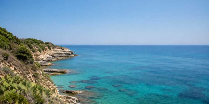 Mare calmo e luminoso lungo una costa italiana sotto il sole estivo, acqua azzurra.