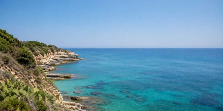 Mare calmo e luminoso lungo una costa italiana sotto il sole estivo, acqua azzurra.