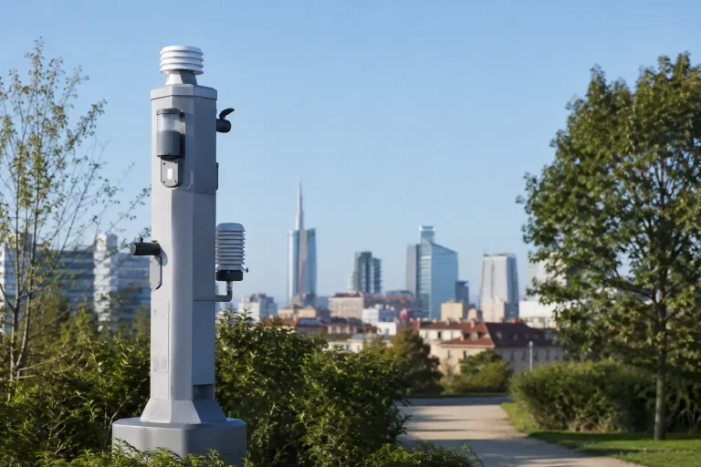 Skyline di una città europea con aria limpida al mattino e una centralina di monitoraggio della qualità dell'aria in primo piano