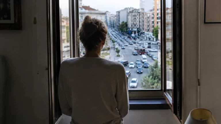 Persona affacciata alla finestra su una strada urbana trafficata e rumorosa