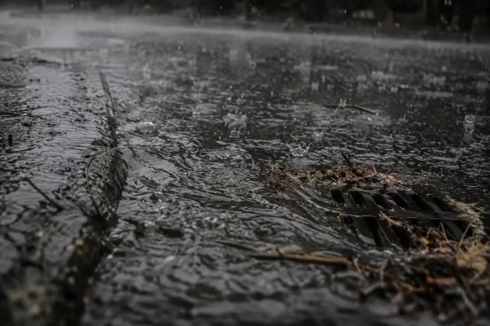 Acquazzone su asfalto urbano: l'acqua scorre in superficie verso un tombino senza infiltrarsi e ricaricare le falde.