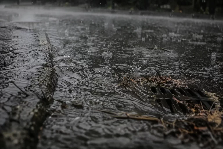 Acquazzone su asfalto urbano: l'acqua scorre in superficie verso un tombino senza infiltrarsi e ricaricare le falde.