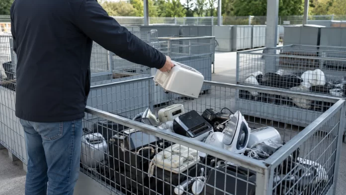 Persona di spalle che deposita un piccolo elettrodomestico in una gabbia per rifiuti elettronici