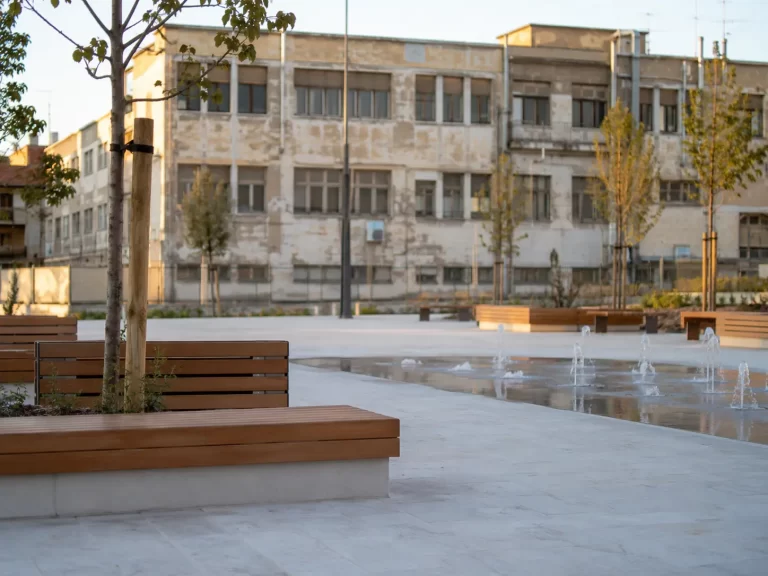 Piazza cittadina riqualificata e, sullo sfondo, una scuola pubblica datata: la rigenerazione urbana del PNRR
